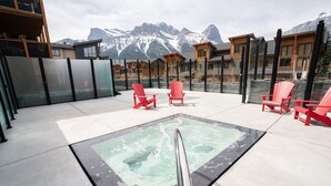 Una terrazza sul tetto con vasca idromassaggio vetrata, poltrone Adirondack rosse e vista sulle montagne.