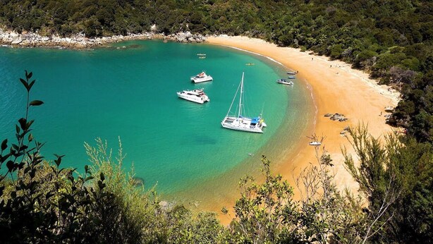 A beach with clear turquoise waters, boats, and a sandy shore surrounded by greenery. - Abel Tasman M arahau (Marahau)
