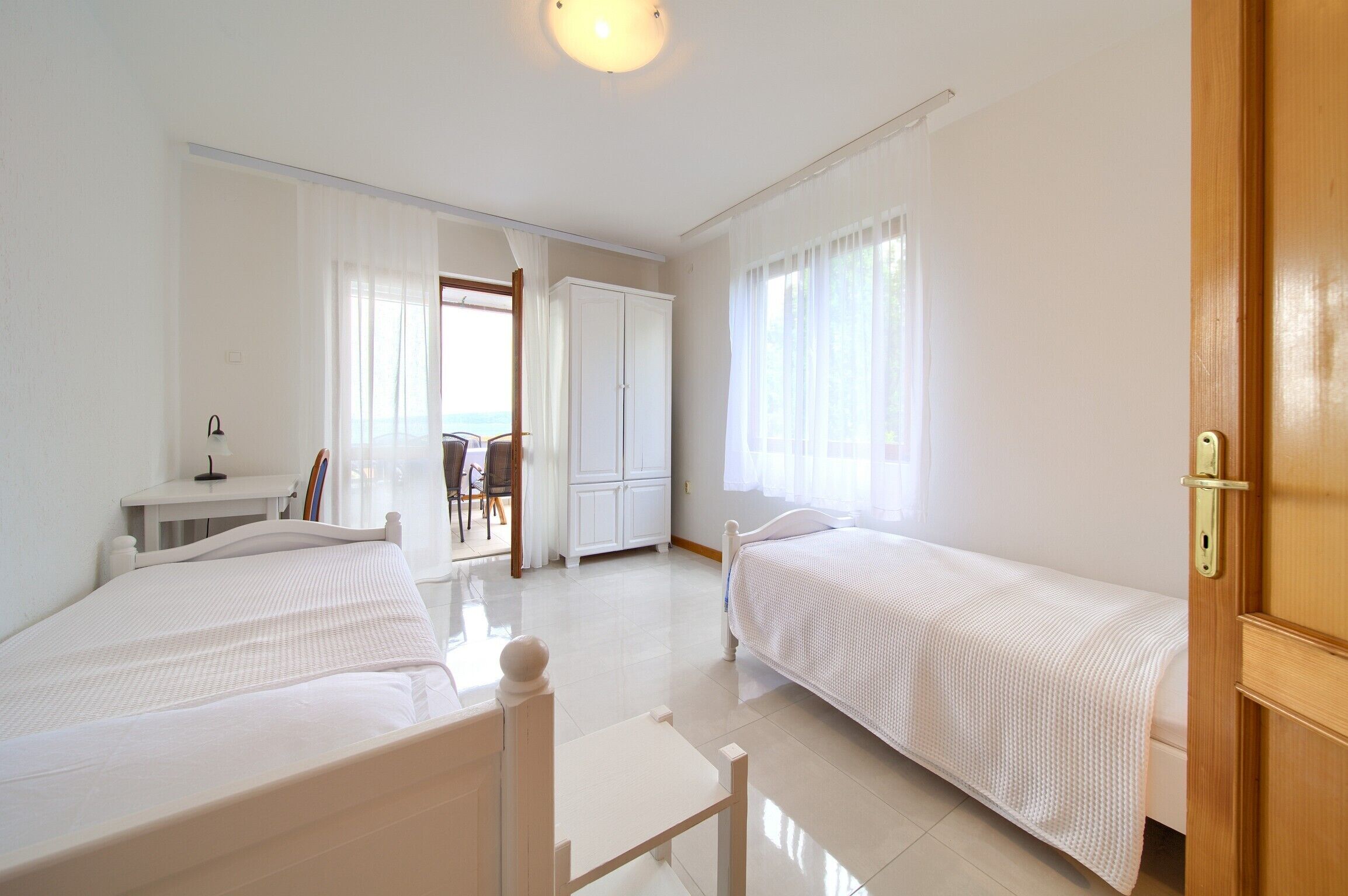 A hotel room with two single beds, a desk with a chair, and a wardrobe.