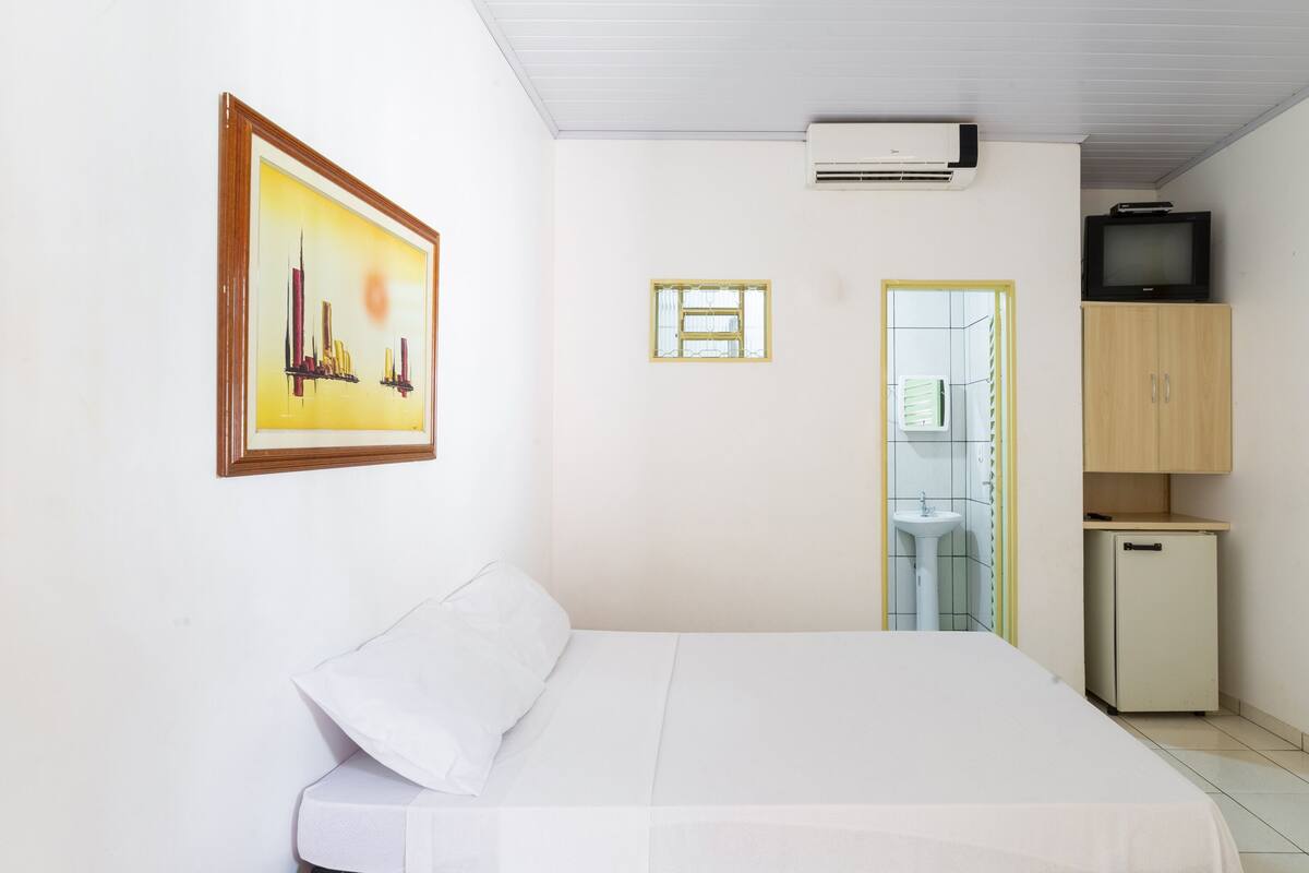 Une chambre avec un lit, un tableau encadré, un climatiseur, une télévision et une petite kitchenette.