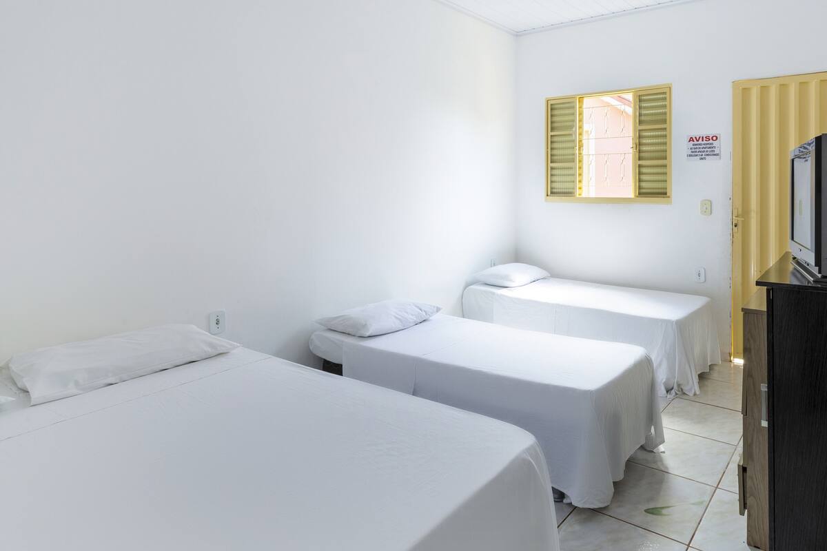 Une chambre avec deux lits simples, un téléviseur posé sur un meuble et une fenêtre équipée de stores.