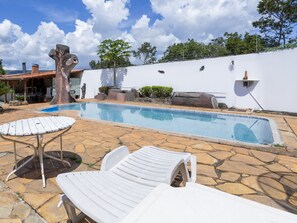 A swimming pool with lounge chairs, a tree sculpture, and a white wall with a chimney. - OYO Pousada LN (Caldas Novas)