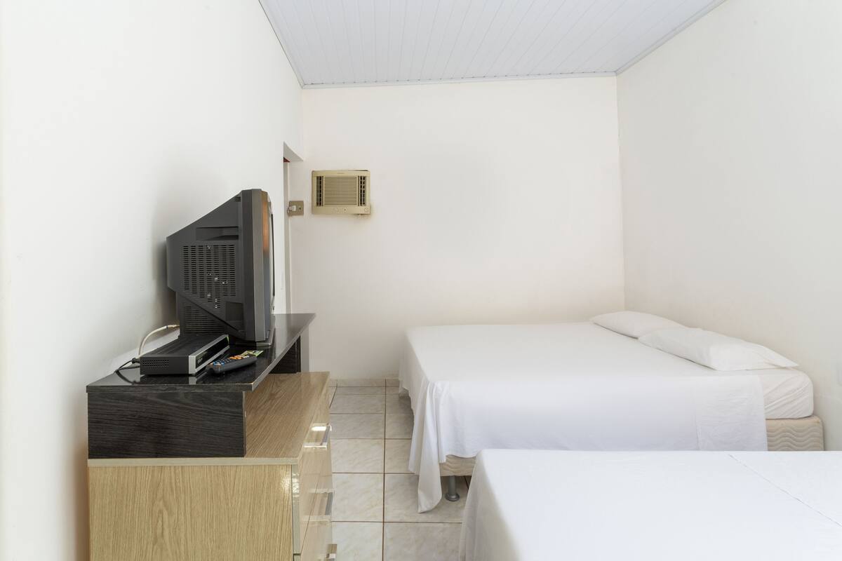 Une petite pièce propre, avec un lit, un bureau équipé d’un ordinateur et un climatiseur fixé au mur.