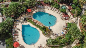 A resort with two oval-shaped swimming pools surrounded by lounge chairs and umbrellas, with palm trees and a landscaped garden. - OCEANVIEW 308 MARGATE - Bright Beach Decor, NEW FLOORS, & Ready to Accommodate!  (Myrtle Beach)
