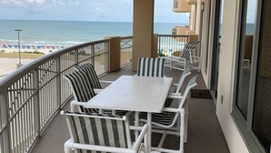 A balcony with a white table and striped chairs, overlooking a beach. - OCEANVIEW 308 MARGATE - Bright Beach Decor, NEW FLOORS, & Ready to Accommodate!  (Myrtle Beach)