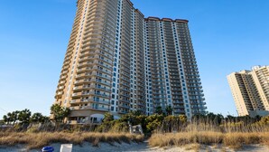 A tall, multi-story hotel with a curved facade, located near a beach with sandy dunes and sparse vegetation. - OCEANVIEW 308 MARGATE - Bright Beach Decor, NEW FLOORS, & Ready to Accommodate!  (Myrtle Beach)