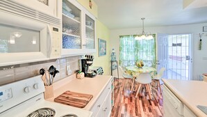 A kitchen with a wooden floor, white cabinets, a stove, and a dining area with a table and chairs.