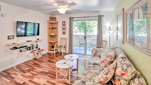 A living room with a flat-screen TV, wooden flooring, a ceiling fan, a floral sofa, and a sliding glass door leading to an outdoor patio.