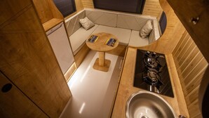 Una cocina compacta con estufa a gas, un lavamanos y una pequeña mesa redonda con libros.