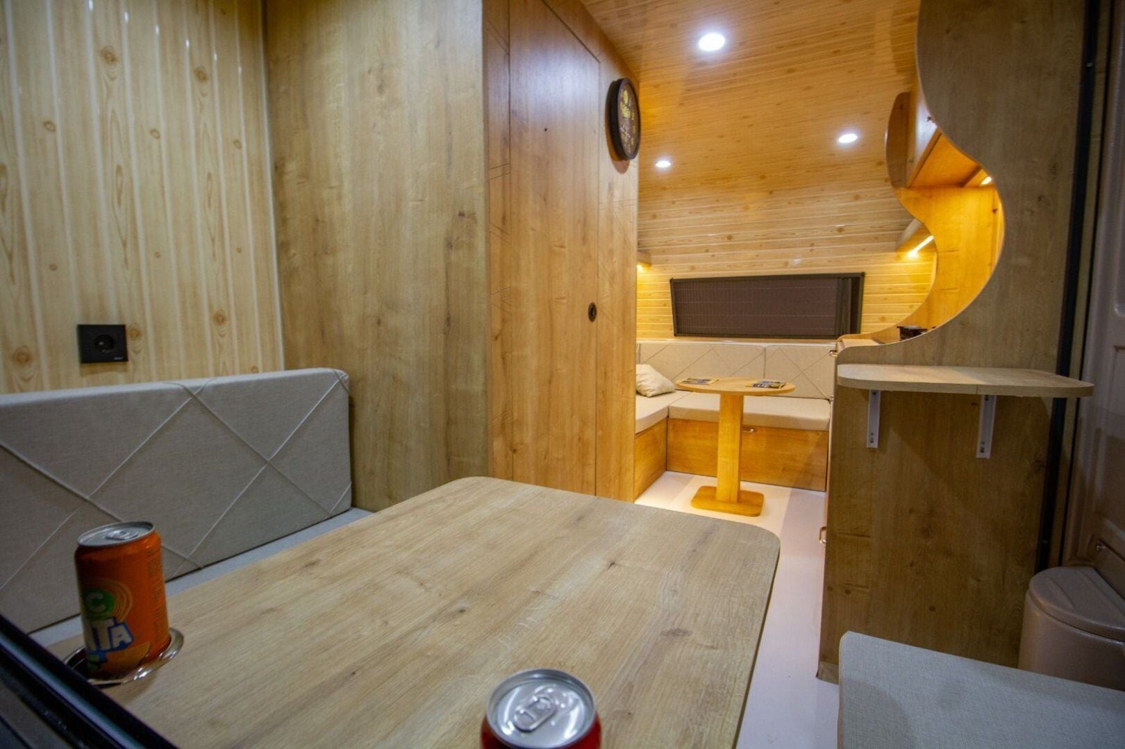 A compact, wooden interior with a dining area, a small seating nook, and a built-in TV.
