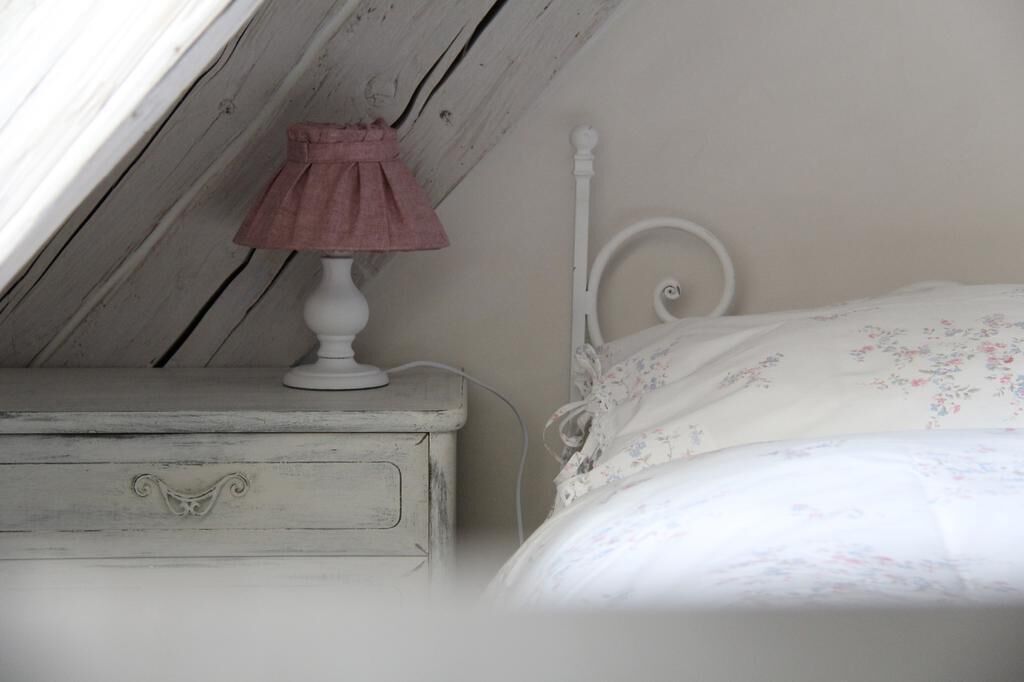 A bedroom with a white bed, a white nightstand with a pink lamp, and a wooden ceiling.