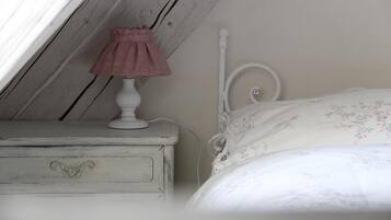 A bedroom with a white bed, a white nightstand with a pink lamp, and a wooden ceiling.