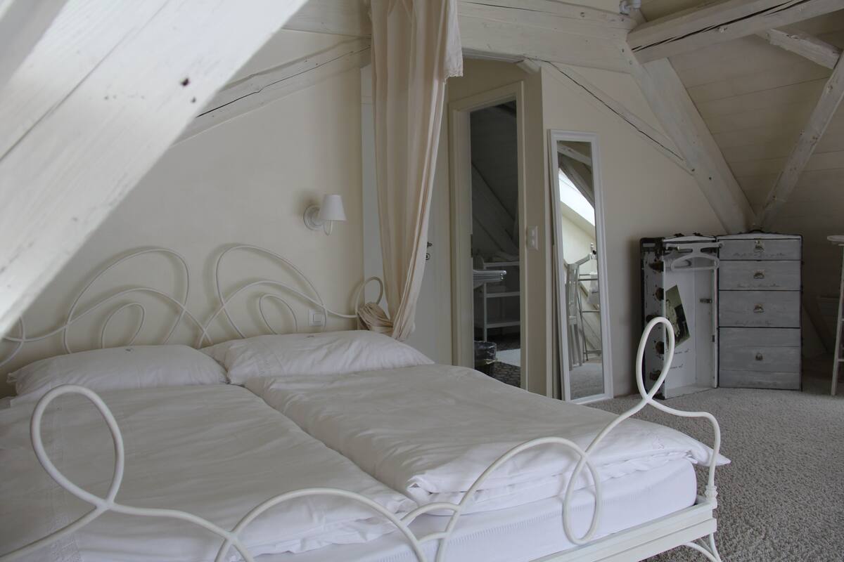 Ein Bett mit Baldachin aus weißem Metall in einem Zimmer mit schrägen Decken und einer weißen Kommode.