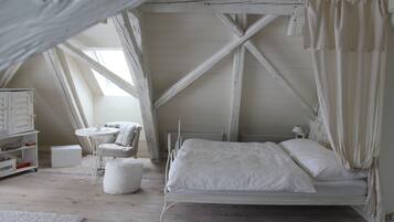 A white, loft-style bedroom with a bed, a small round table, and a chair.