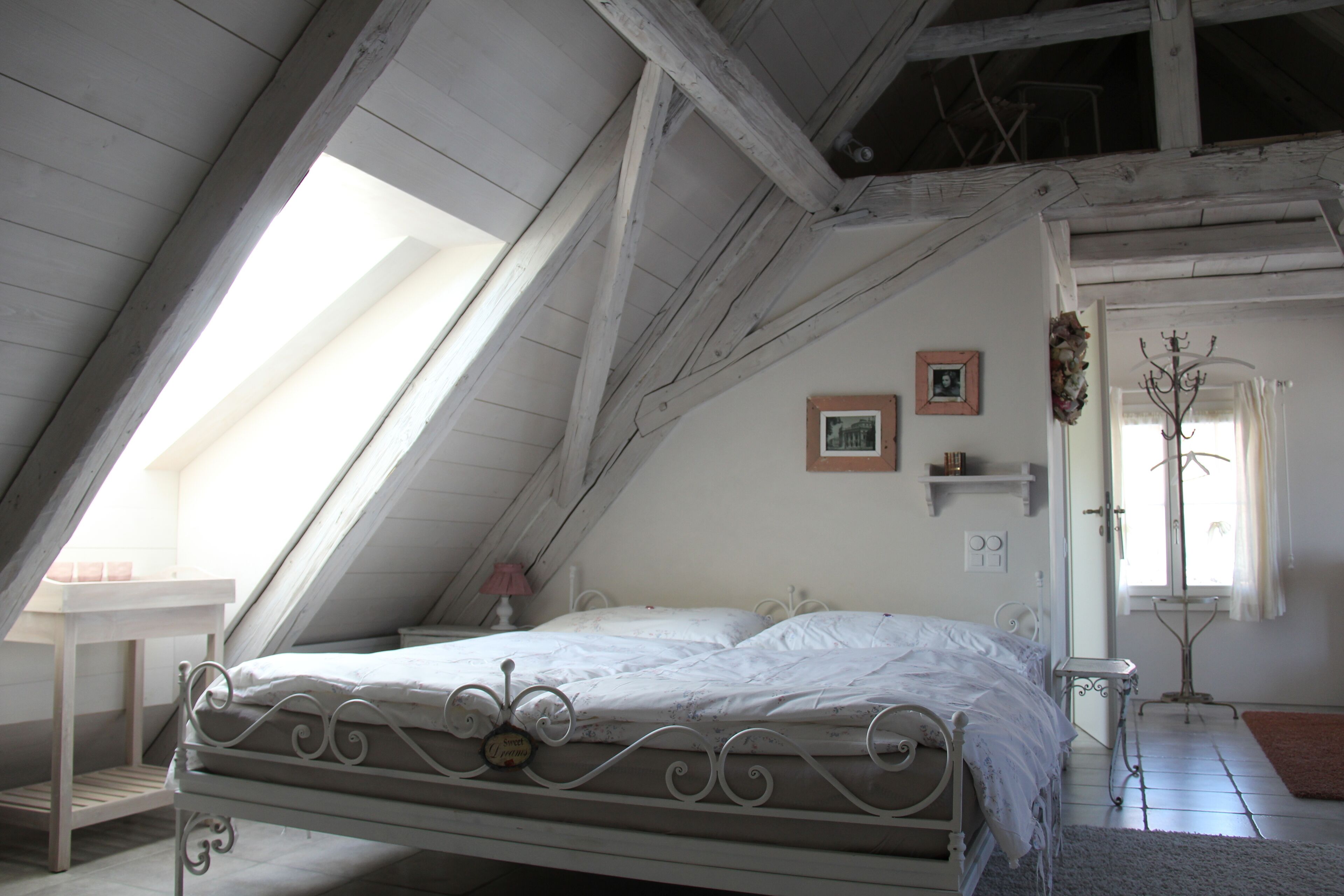 A bedroom with a sloped ceiling, a bed, a small table, and a window.