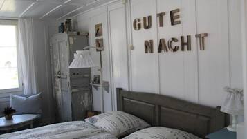 A bedroom with a bed, pillows, a nightstand, a dresser, and a wall with 'GUTE NACHT' letters.
