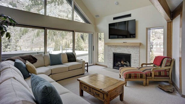 Un salón amplio con un gran ventanal, chimenea, televisión y asientos cómodos.