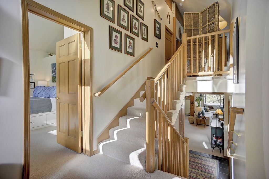 A staircase with wooden railings leading to a second floor, a hallway with framed pictures, and a room with a bed and a window.