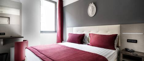 A modern hotel room with a large bed, a desk with a telephone, and a wall-mounted clock.