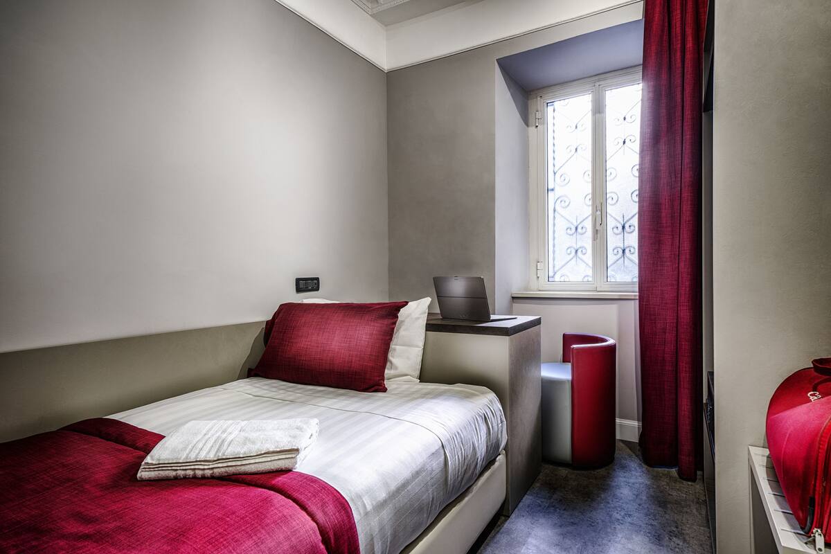 A bedroom with a bed, a desk, a chair, and a window with curtains.