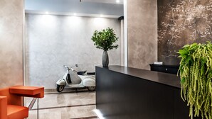 A modern reception area with a marble floor, a reception desk, a white scooter, a vase with green plants, and a wall with a map. - Hotel Varese Roma (Rome)