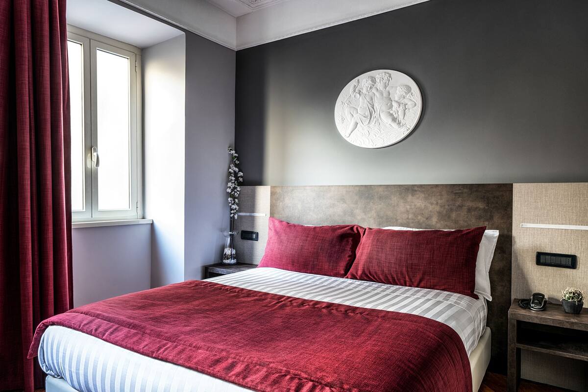 A modern bedroom with a large bed, a round wall decoration, and a nightstand with a phone and a small plant.