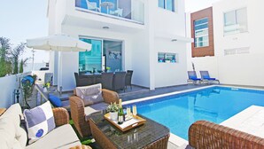 A modern outdoor pool area with wicker furniture, a glass balustrade, and a dining setup with chairs and tables.