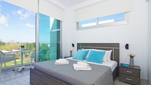 A modern bedroom with a large bed, two nightstands, a small table, and a balcony with a view.