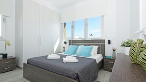 A modern bedroom with a large bed, bedside tables, a nightstand, and a view of the sky through the window.