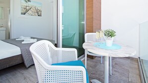 A hotel room with a bed, a seating area with a table, a potted plant, and a glass door leading to a balcony.