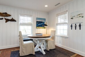 A dining area with a round table, two striped chairs, a painting, and a lamp.