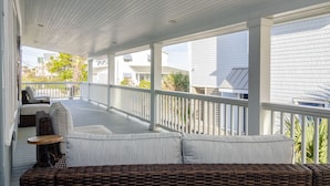 A covered porch with wicker furniture, a cushioned seating area, and a view of neighboring houses.