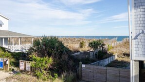 A beach house with a wooden deck, a fenced area, and a view of the ocean.