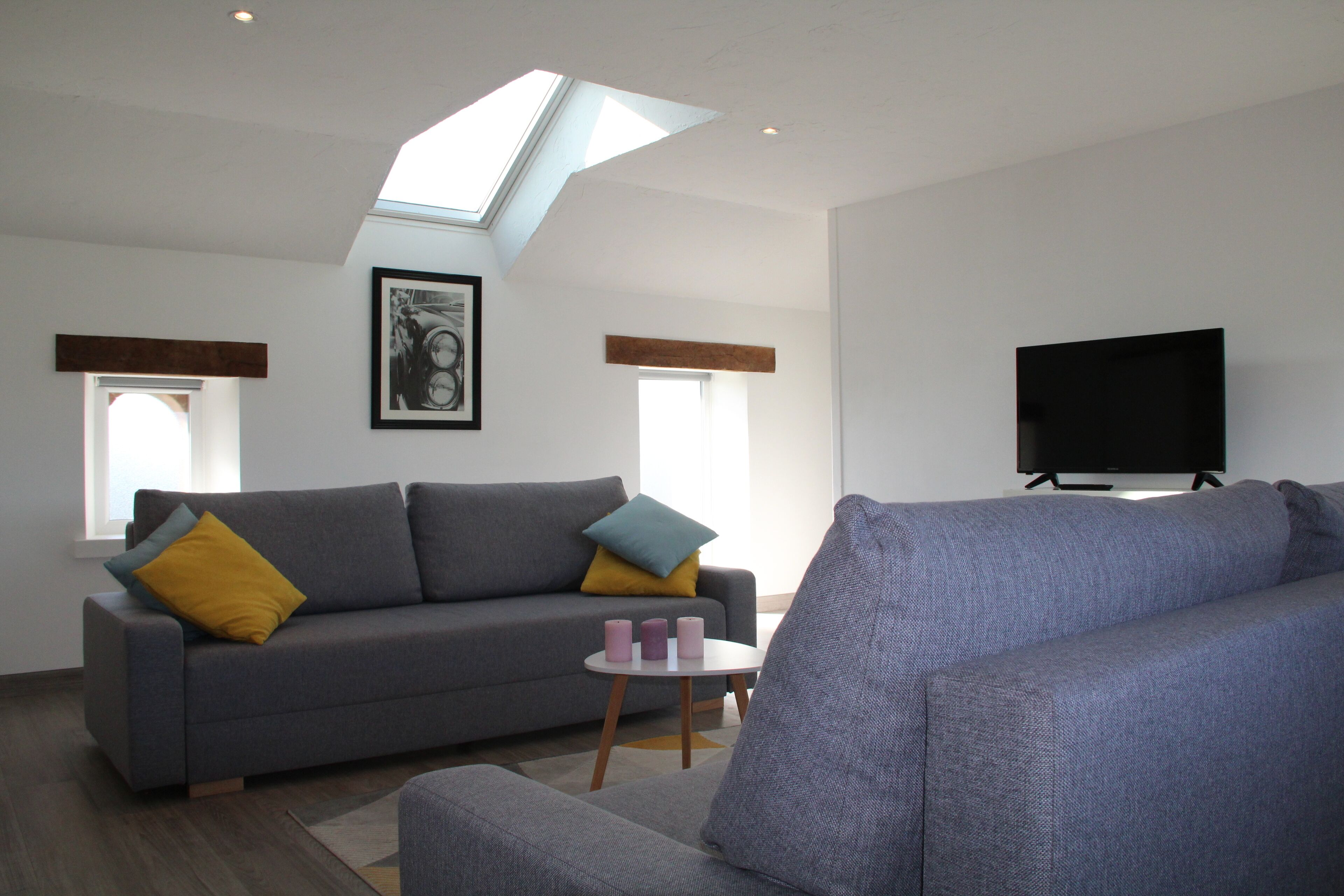 A modern living room with a grey sofa, a small side table, a television, and a skylight.