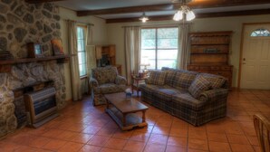 A cozy living room with a stone fireplace, a plaid sofa, a wooden coffee table, and a television.