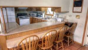 A kitchen with wooden cabinets, a microwave, a stove, a sink, and a bar area with four wooden chairs.