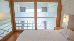 A hotel room with a large bed, a wooden headboard, a nightstand, and a view through a glass door. - The CEO Executive Office Suites (George Town)