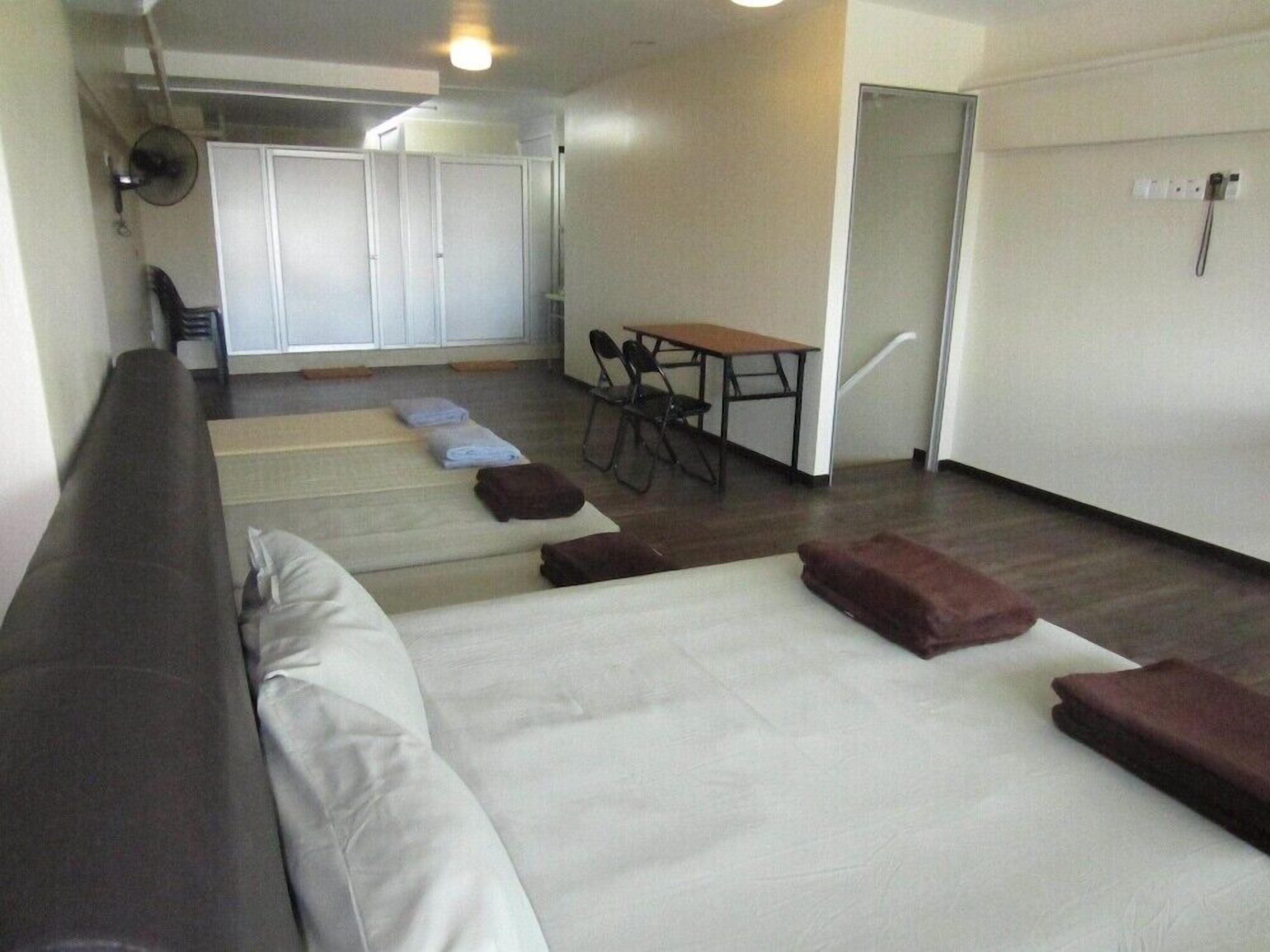 A spacious room with a large bed, a sofa, a dining table with chairs, and a small table with a fan.
