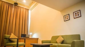 A room with a green sofa, a green armchair, a small table, a desk with a laptop, and a window with curtains. - The CEO Executive Office Suites (George Town)