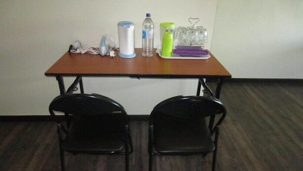 A small room with a wooden table and two black chairs. On the table, there are a water bottle, a green container, a white container, and a purple tray with glasses. - The CEO Executive Office Suites (George Town)