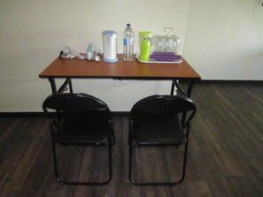 A small room with a wooden table and two black chairs. On the table, there are a water bottle, a green container, a white container, and a purple tray with glasses. - The CEO Executive Office Suites (George Town)