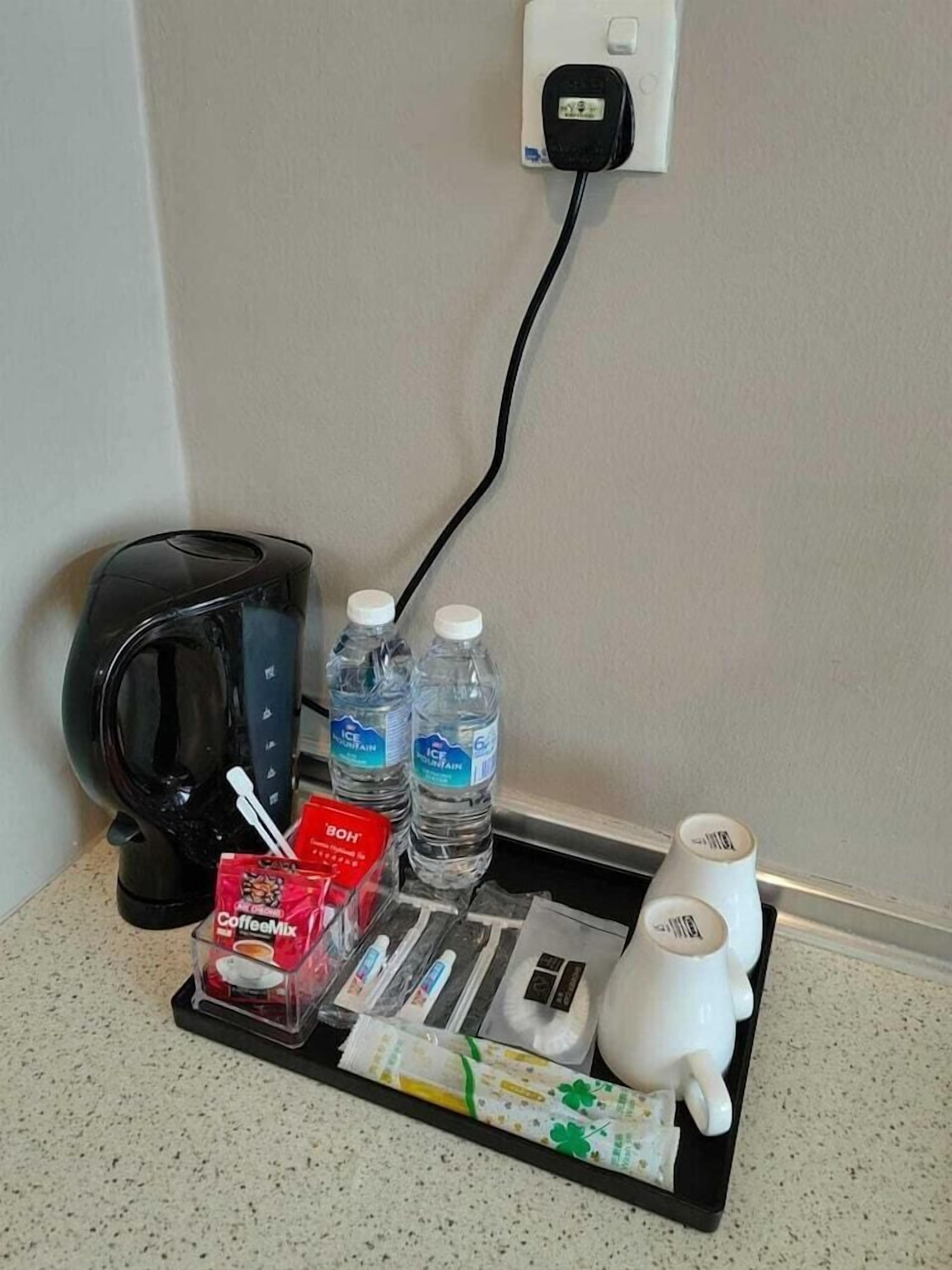 A coffee maker, two bottles of water, a coffee packet, a tea packet, and a white mug on a tray.