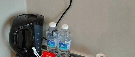 A coffee maker, two bottles of water, a coffee packet, a tea packet, and a white mug on a tray.