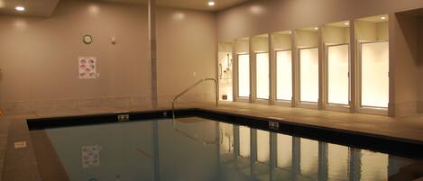 An indoor swimming pool with clear water, a clock on the wall, and a poster.