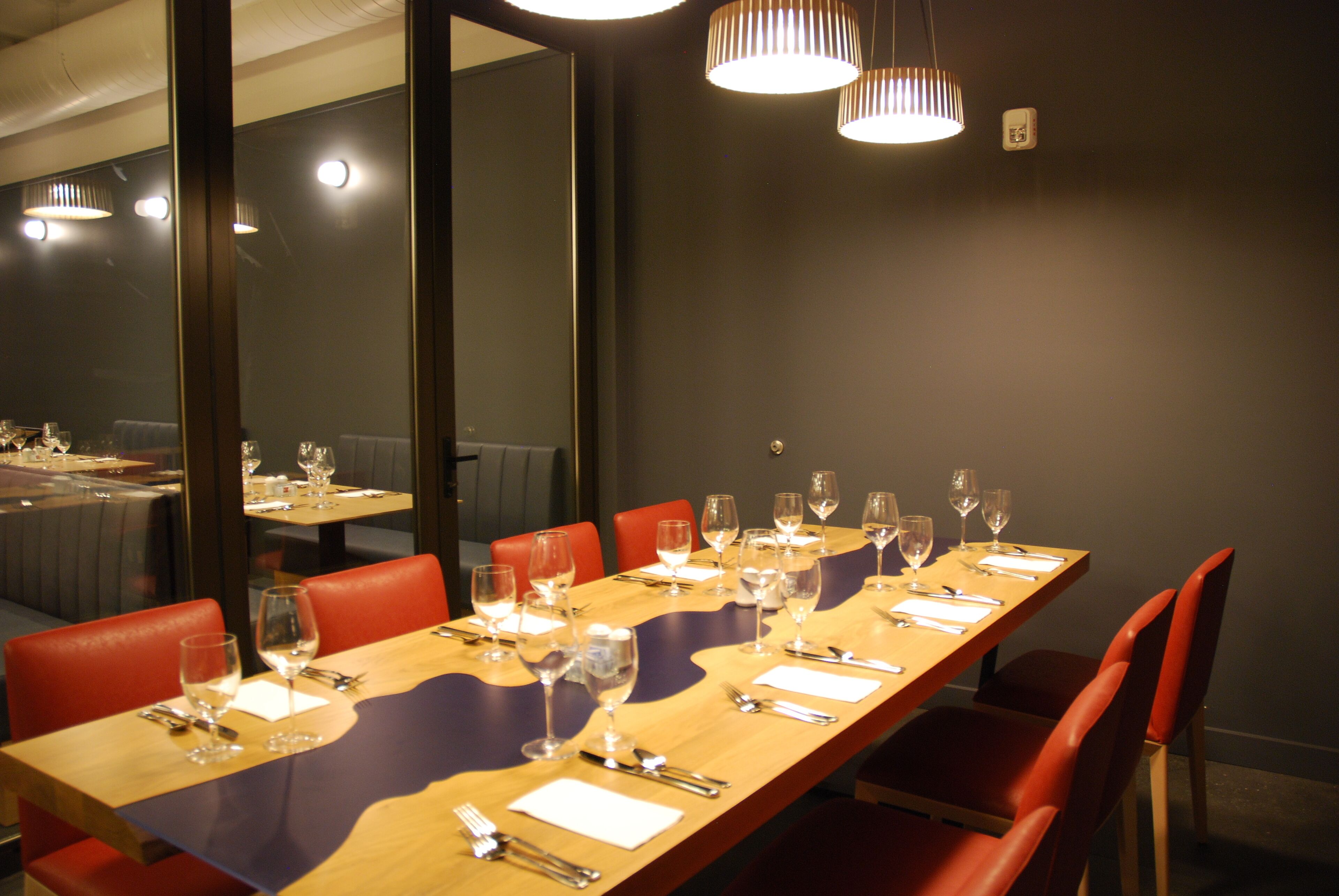 Una larga mesa de comedor dispuesta con varias sillas, vasos y cubiertos, mostrando una disposición formal para comer.
