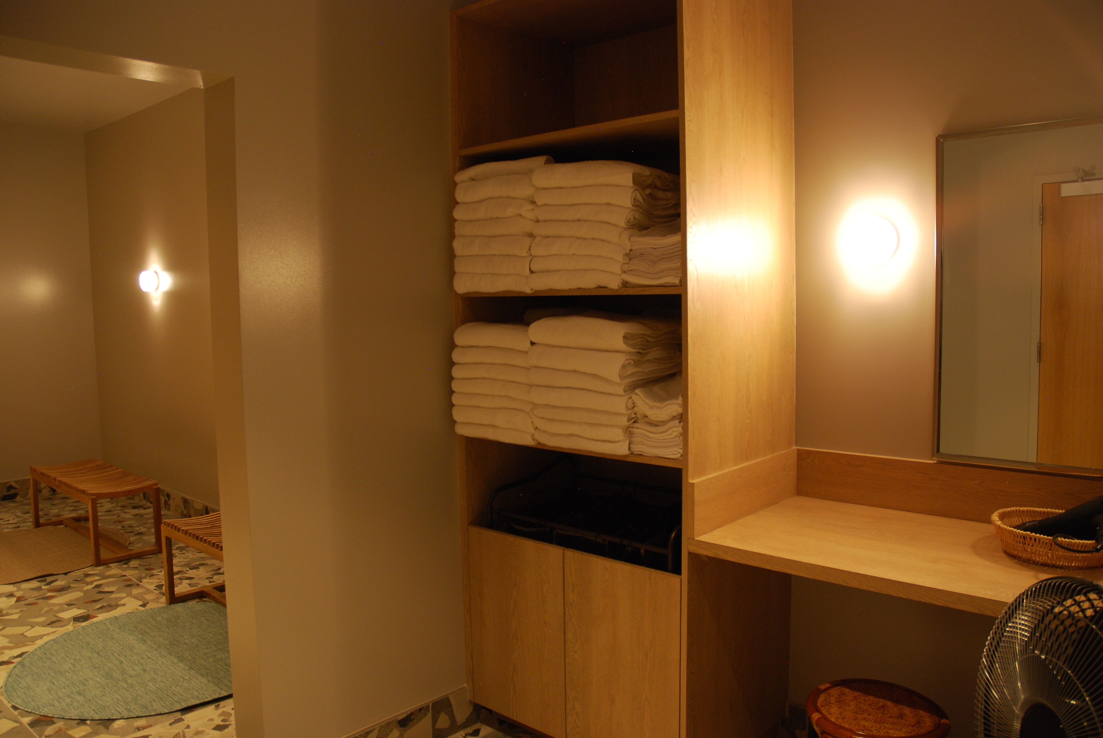 Ein Badezimmer mit einem Holzkosmetikschrank, einem Spiegel, einem Handtuchhalter und einem kleinen Holzschemel.