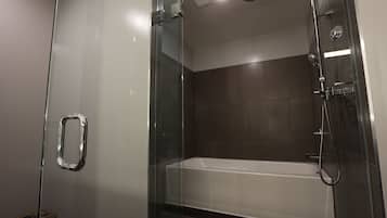 A modern bathroom with a glass-enclosed shower, a white bathtub, and a tiled floor.