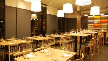 A restaurant with multiple tables set for dining, featuring wooden furniture and hanging pendant lights.