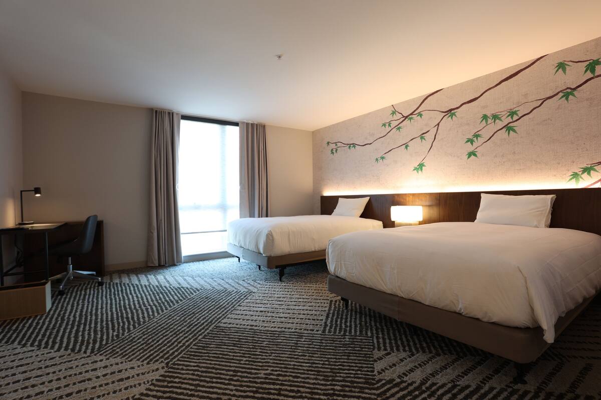 A hotel room with two beds, a desk, and a large window with curtains.