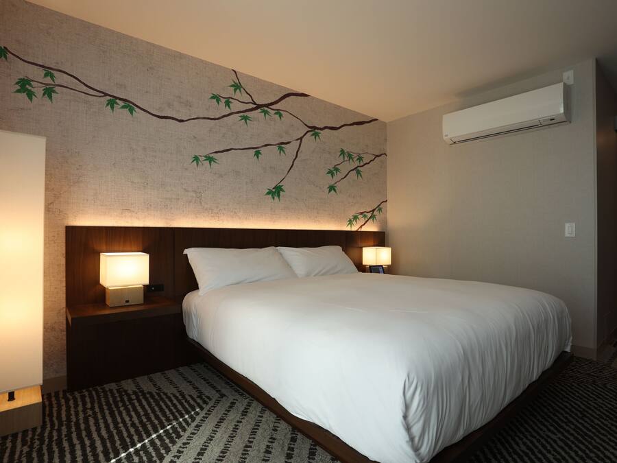Quarto de hotel com uma cama grande, duas luminárias de cabeceira, ar condicionado fixado na parede e um tapete estampado.